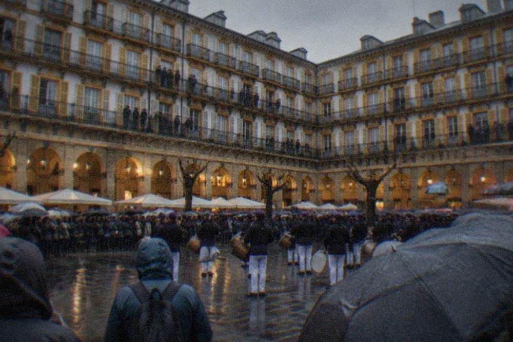 Crowds filling a decorated square with balconies while a drum company performs below
