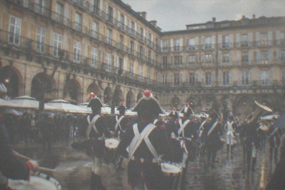 Rows of drummers in period military costume with brass instruments on a city street