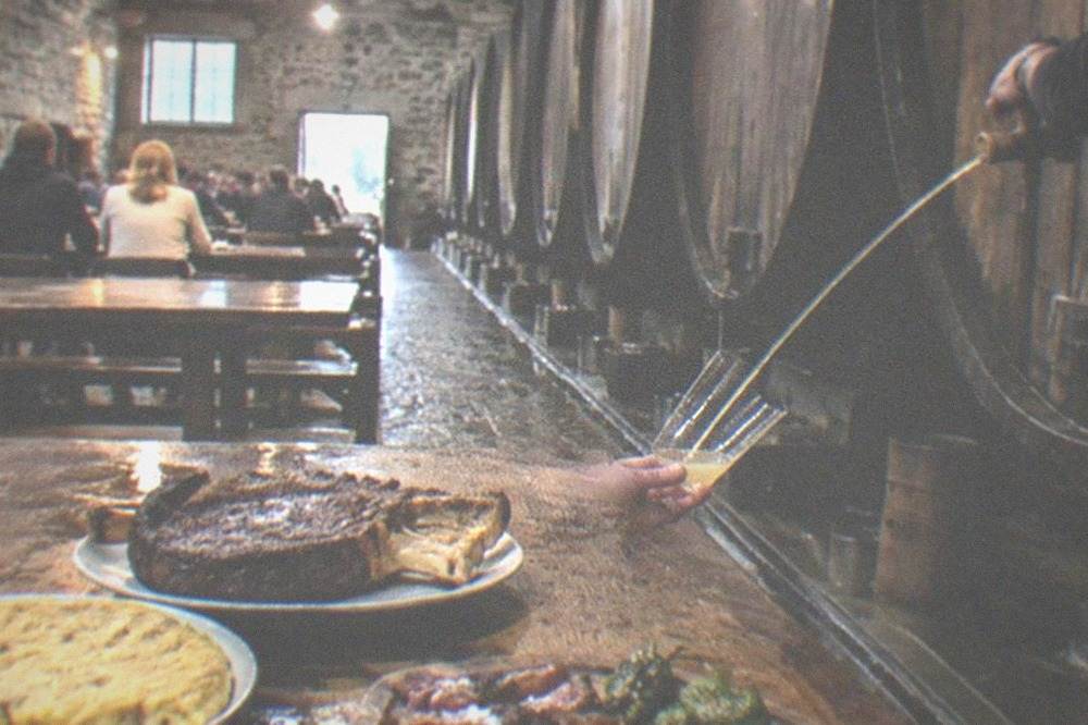 A wooden board of sliced bone-in rib steak with roasted green peppers on a cider house table