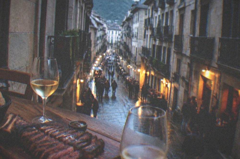 An evening table in a Basque grill restaurant with a steak board, glasses of white wine and bread