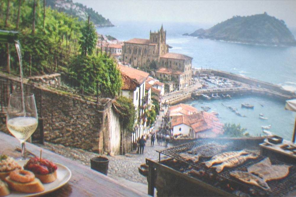 A glass of txakoli being poured from a height beside a plate of pintxos