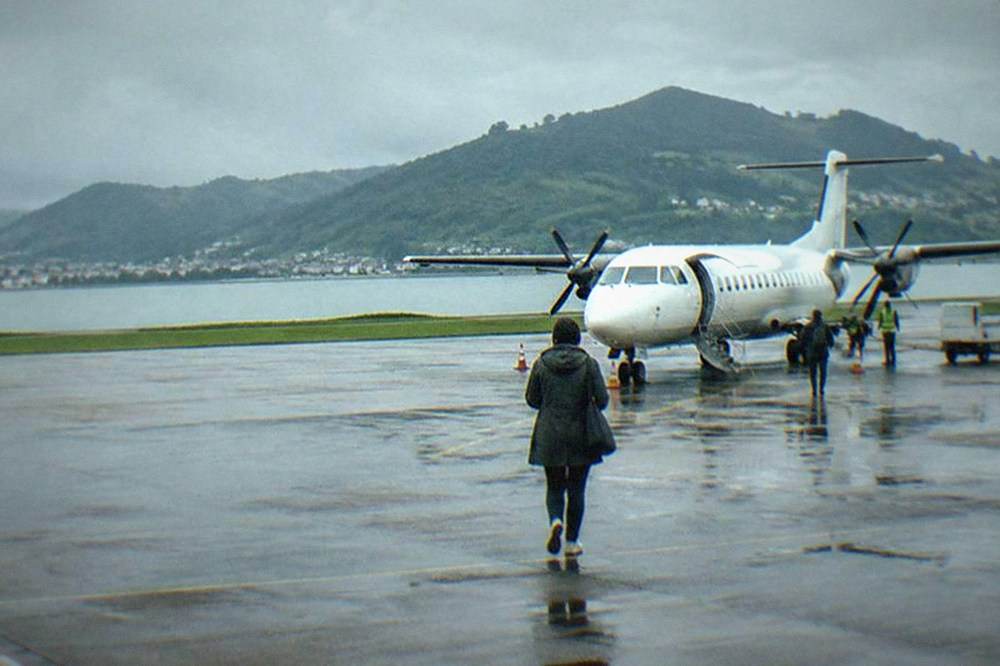 A turboprop aircraft parked at a small airport gate near green hills