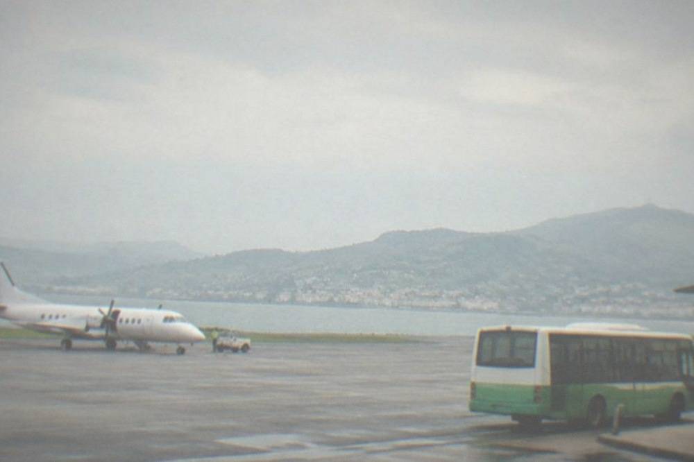 A green and white regional bus waiting at an airport curb