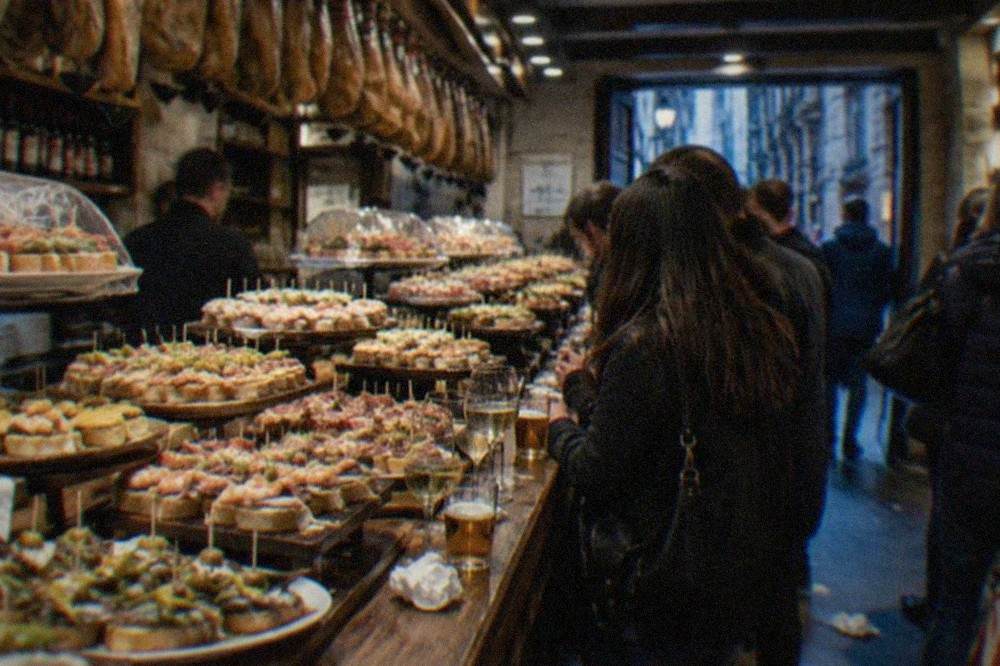 Pintxo bars with crowded counters and hanging seran wrap covered plates in the Old Town of San Sebastián