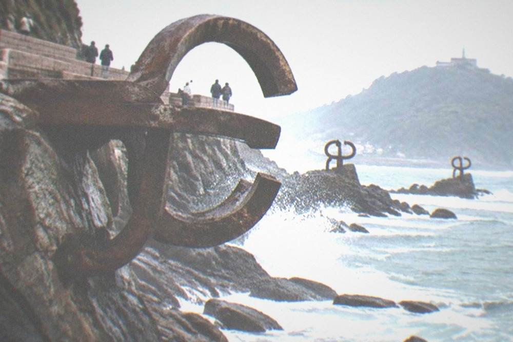 The three steel sculptures of the Peine del Viento standing on wet rocks at the base of Monte Igueldo