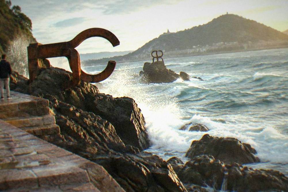 Curved steel sculptures of the Peine del Viento standing on wet rocks at the sea's edge