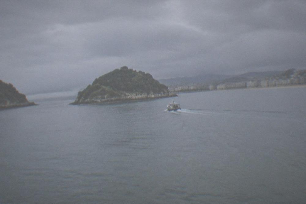 A small boat crossing La Concha bay towards the green island of Santa Clara