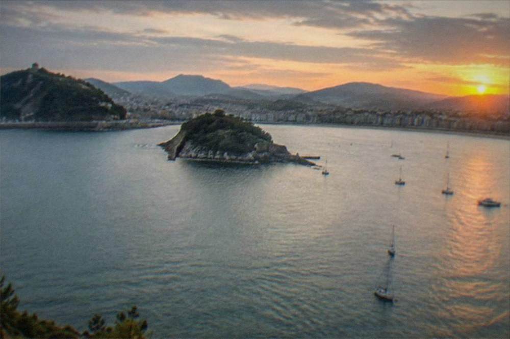 The sun setting over La Concha bay with boats on the water and hills silhouetted