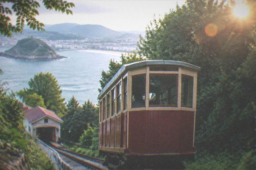 A wooden funicular car climbing the wooded slope of Monte Igueldo above the bay