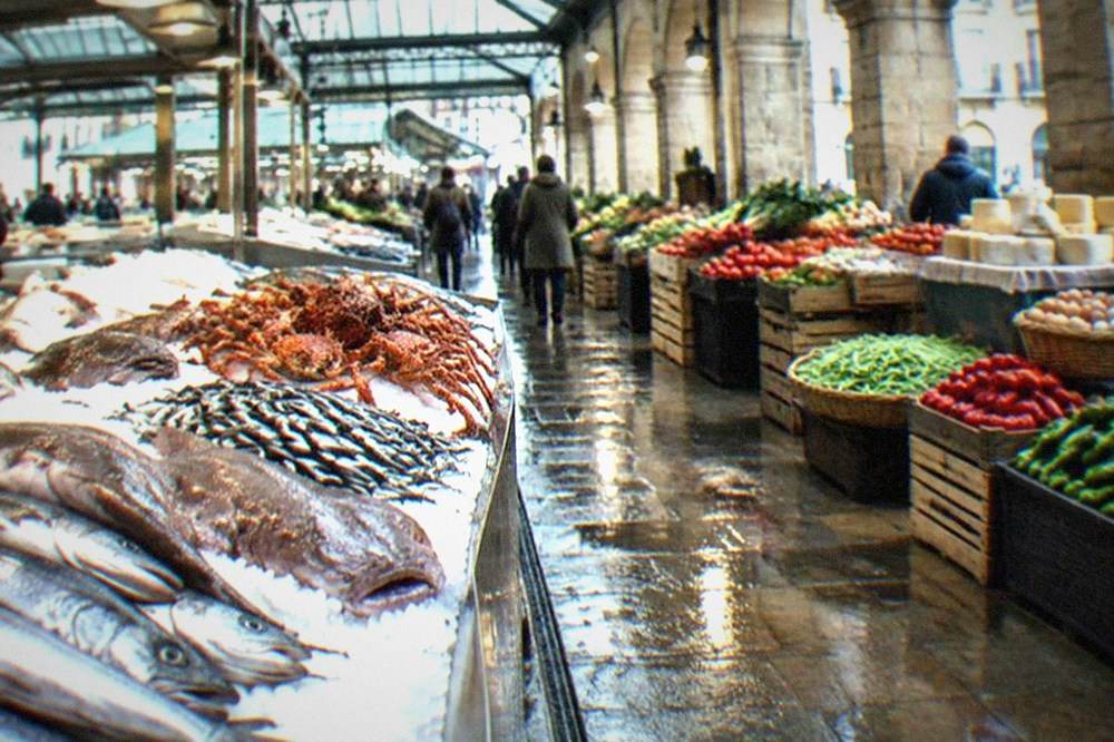 A covered market hall with produce stalls under a glass roof