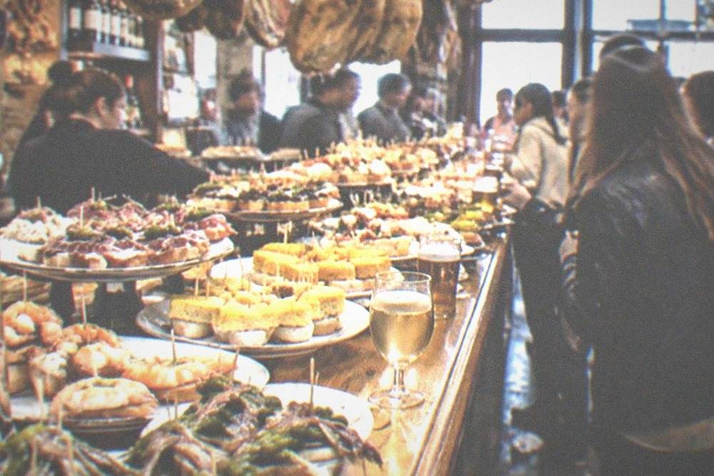 A busy pintxo bar counter with plates of small skewered snacks