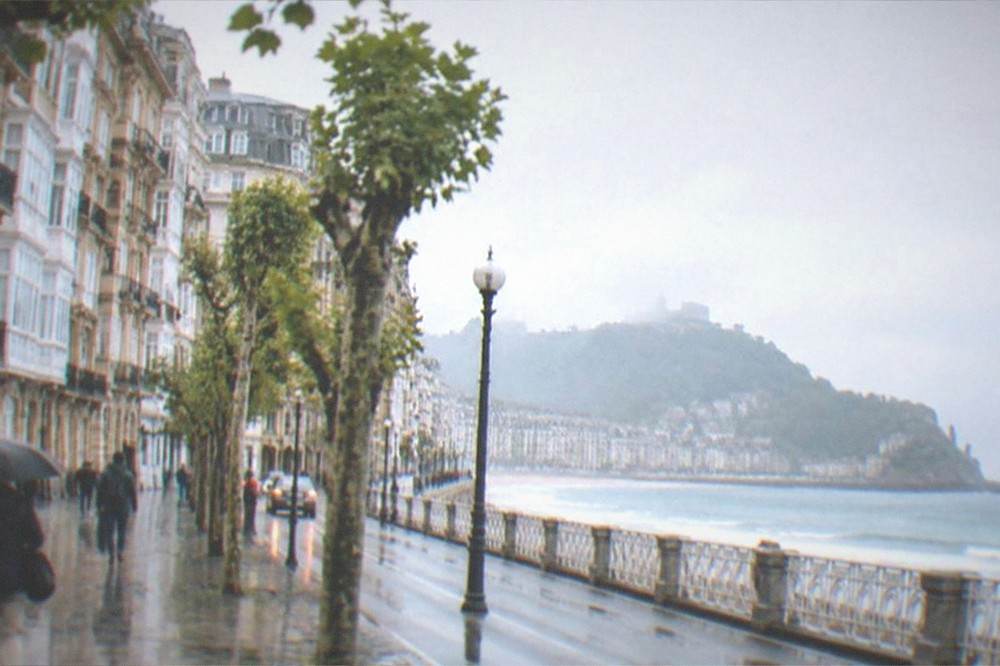 A coastal road with rain clouds over the sea and a distant town