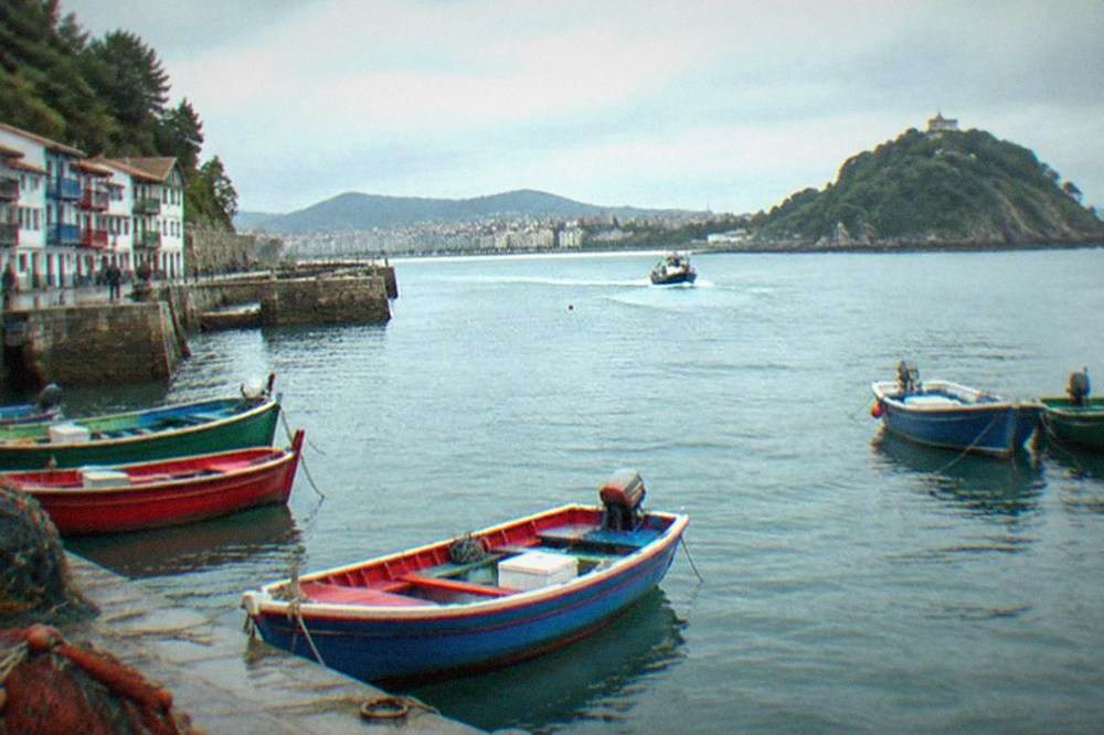A small boat crossing the bay toward the green island with the city behind it
