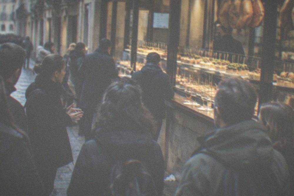 A guide speaking to a small group in a narrow Old Town street with bar counters behind glass