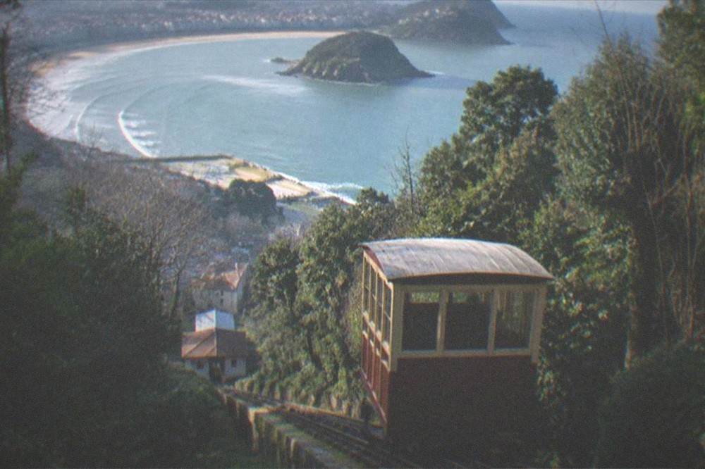 A wooden funicular car climbing a wooded hillside above the bay