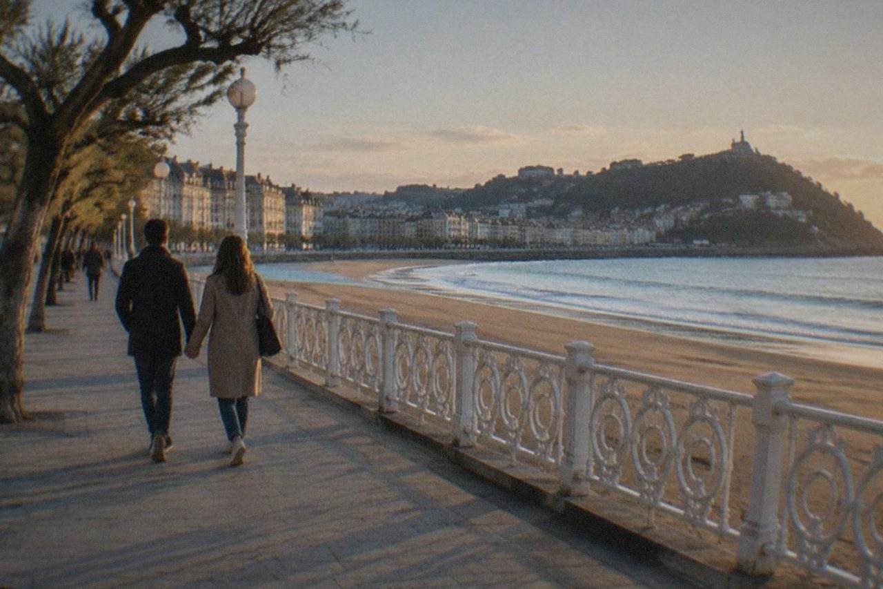 A couple walking hand in hand along the La Concha promenade in San Sebastián at golden hour
