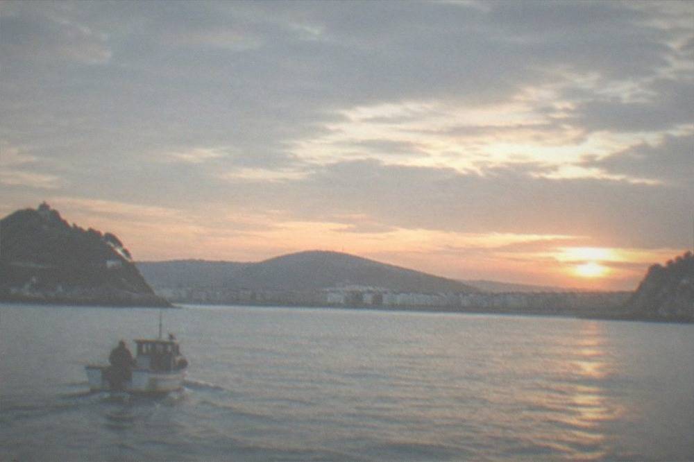 A small boat at sunset on the water outside La Concha bay with cliffs in the distance