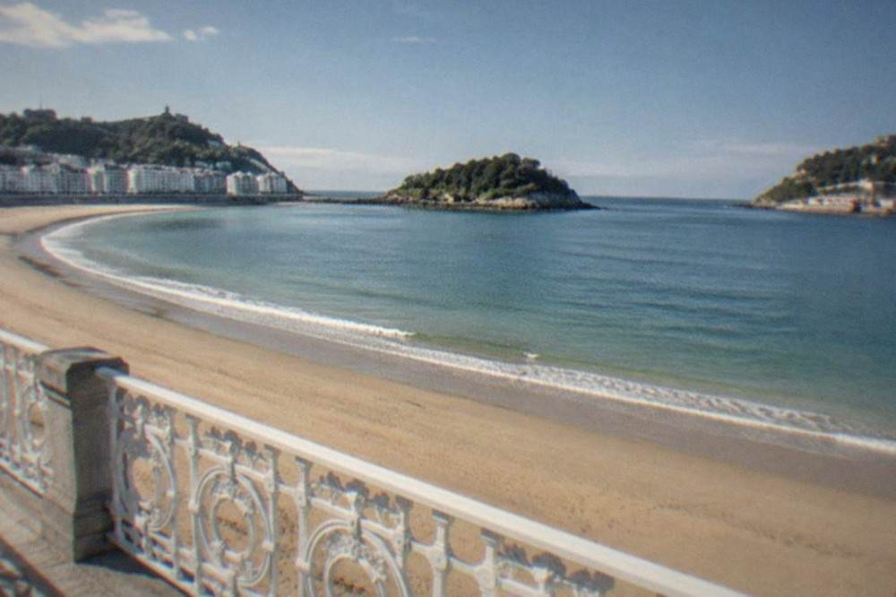 The sandy curve of La Concha beach with the railing and island in morning light