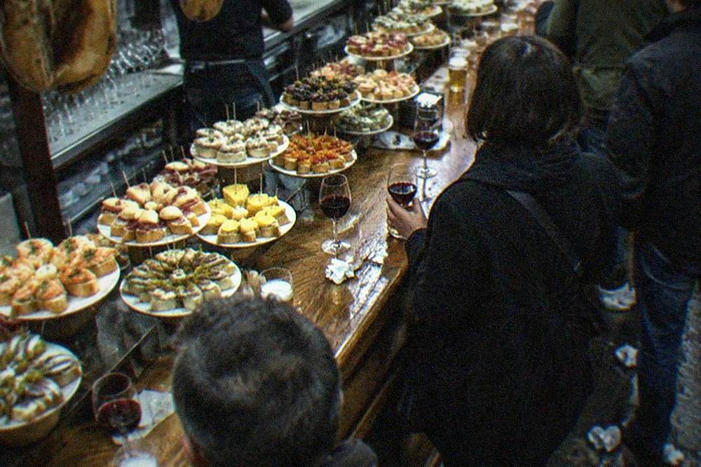 A pintxo bar counter in the Old Town with small skewered dishes and glasses of wine