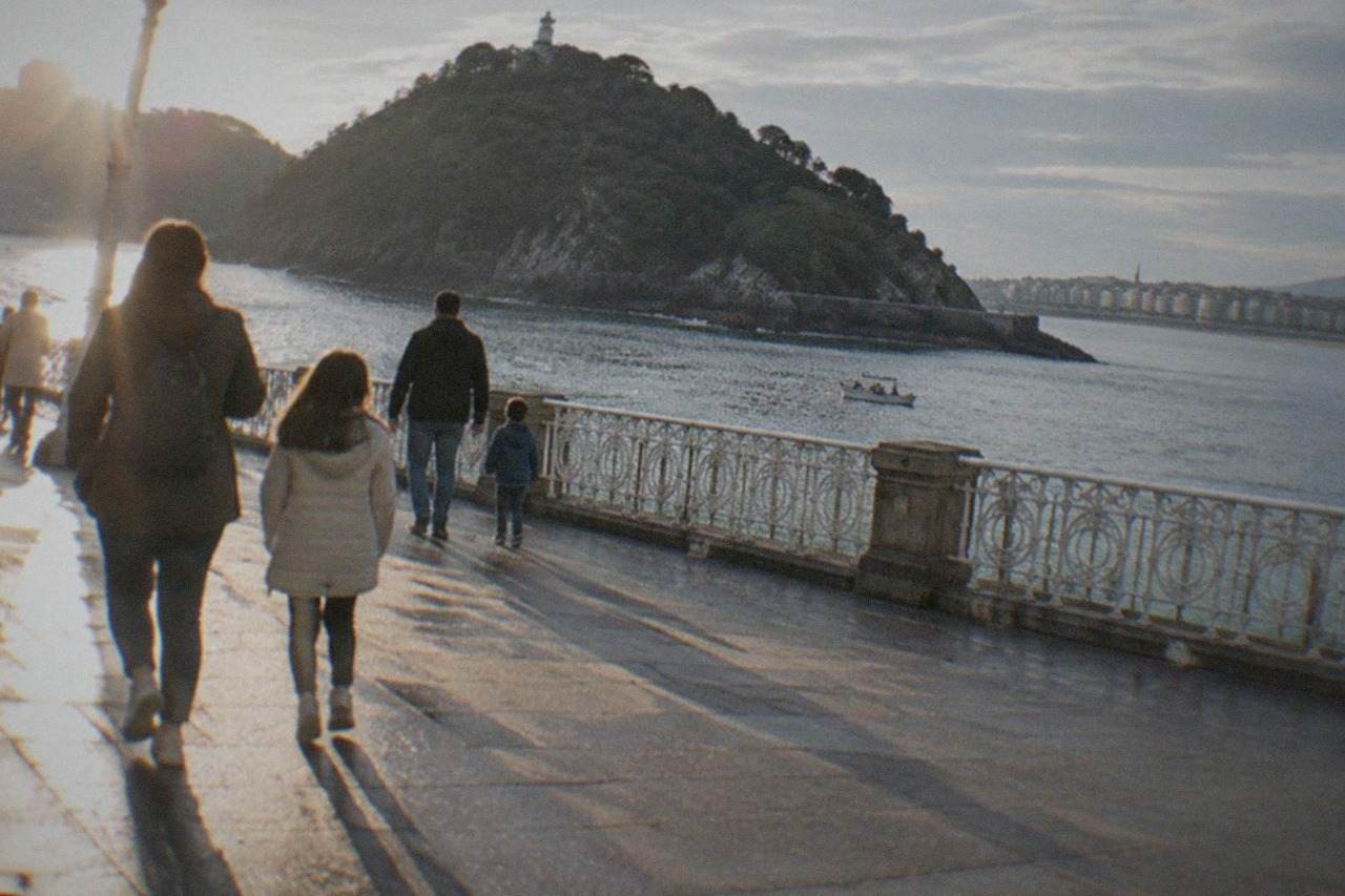 Families walking along the La Concha promenade in San Sebastián with the bay and Santa Clara island behind them