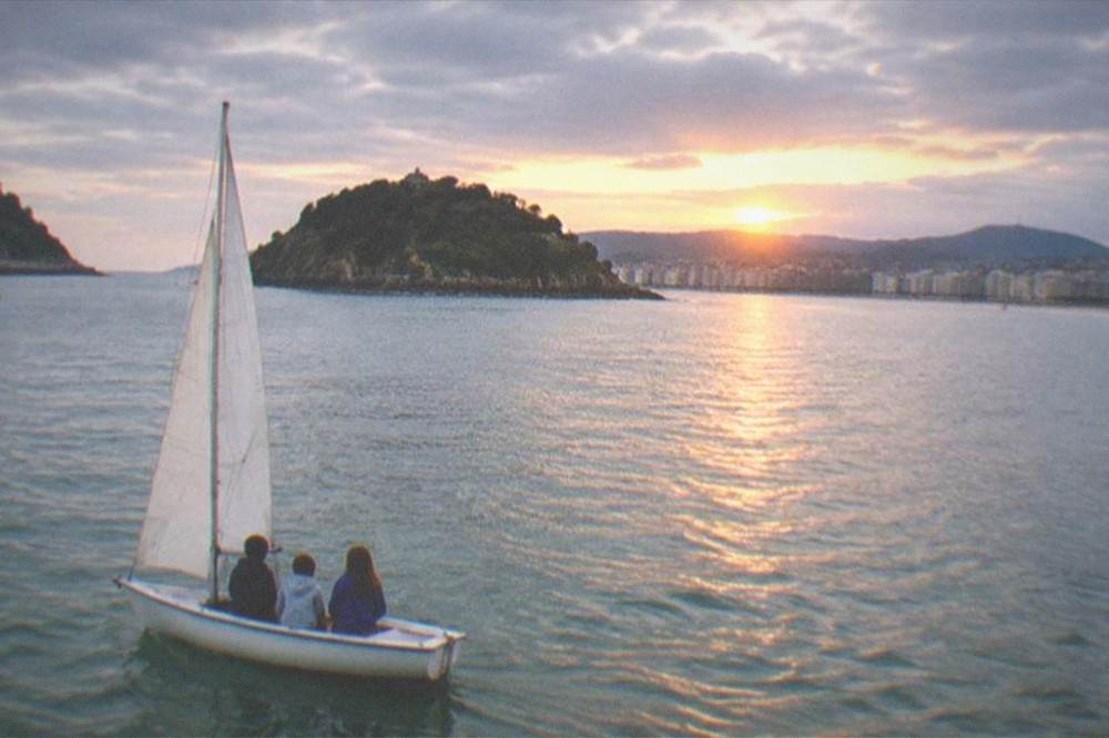 Children watching the sunset from a small sailboat on La Concha bay in San Sebastián