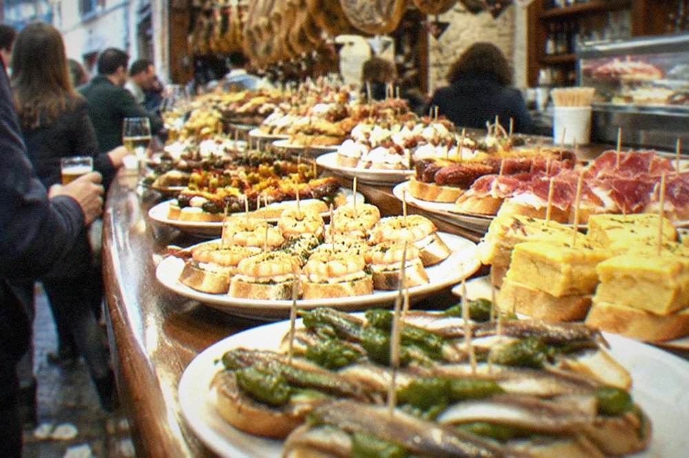 Pintxo bars with crowds standing at the counter in an Old Town street in San Sebastián at night