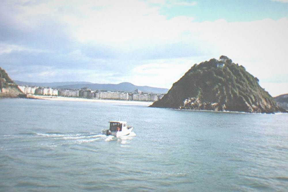 A small boat crossing La Concha bay toward Santa Clara island with the city behind it