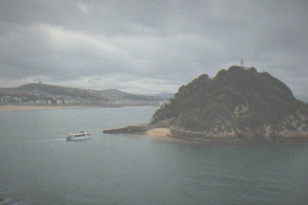 The long curved sandy beach of La Concha with white railing promenade and island in the bay