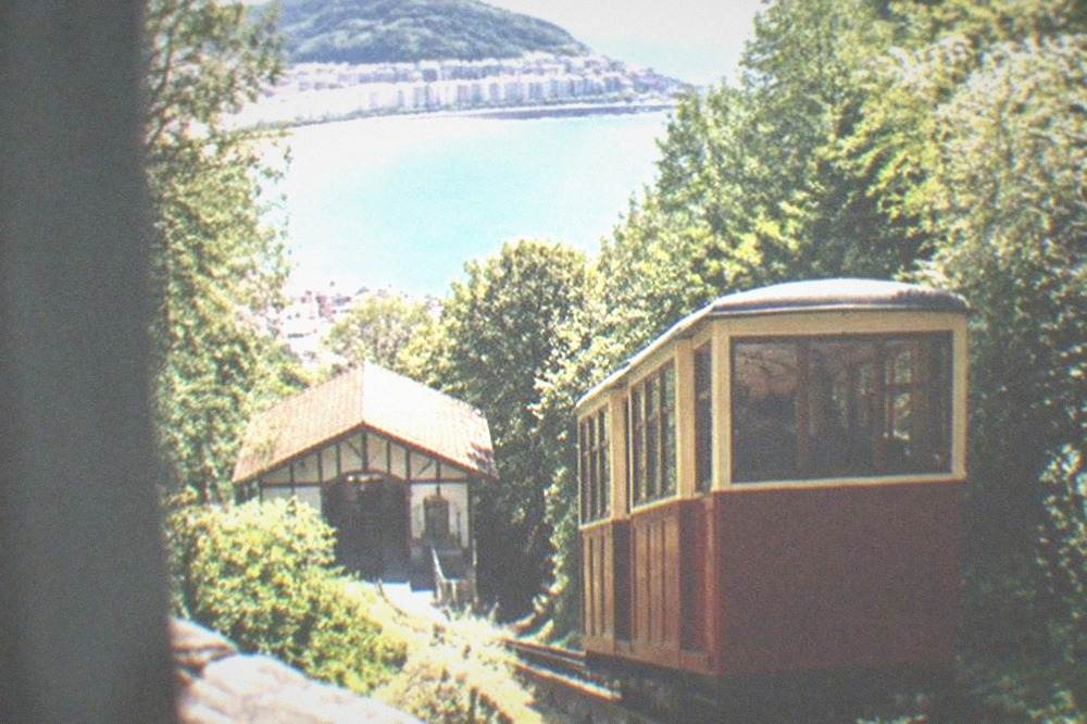 A vintage wooden funicular car climbing the wooded slope of Monte Igueldo above the bay
