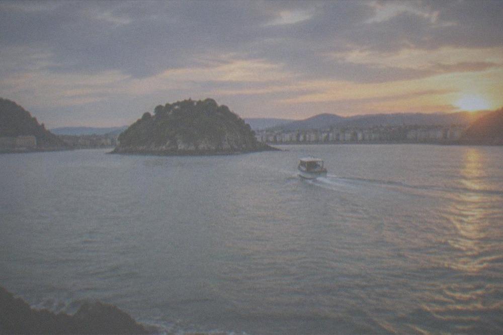 A small boat crossing La Concha bay toward Santa Clara island at golden hour
