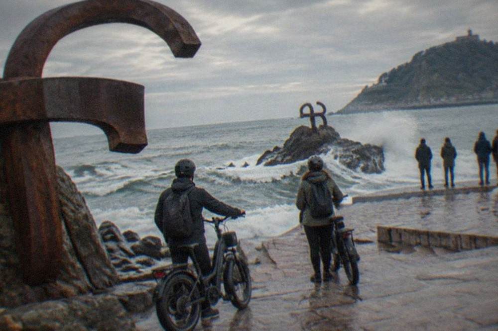 Riders on electric bikes stopping at the Peine del Viento sculptures on a cloudy day