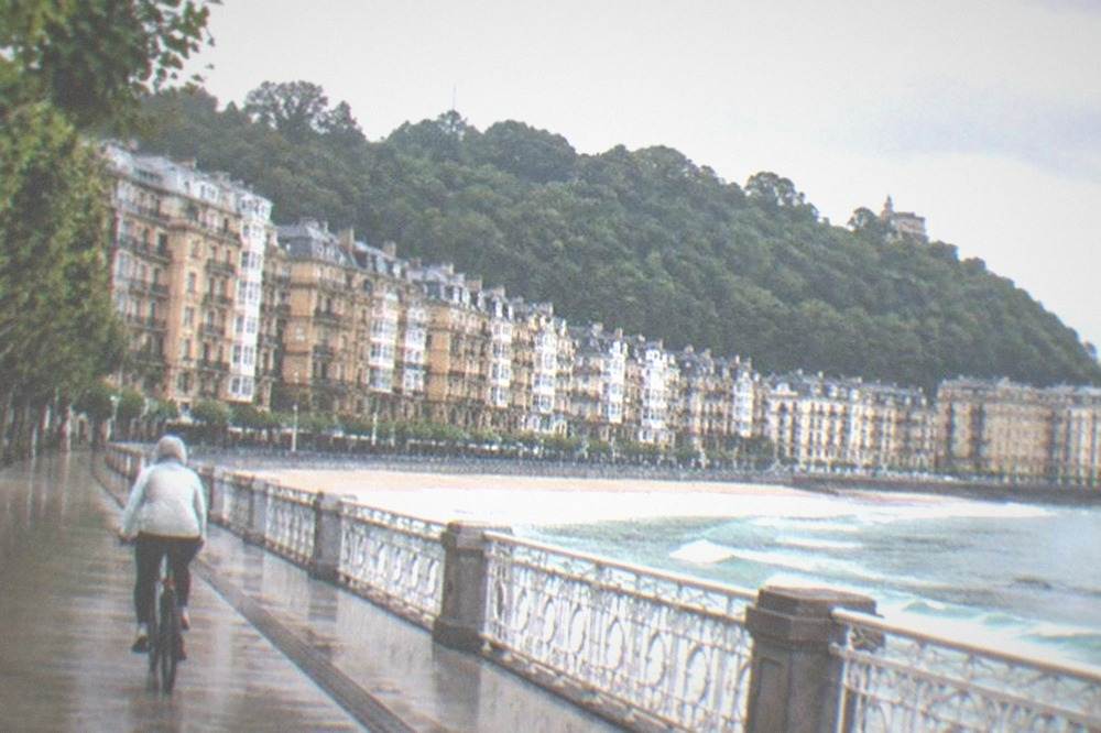 A cyclist in a light rain jacket riding an empty seafront path in San Sebastián