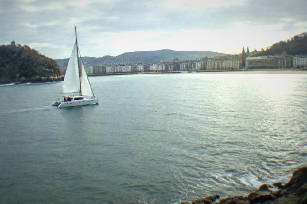 A catamaran sailing across La Concha bay with the curved beach and city behind it