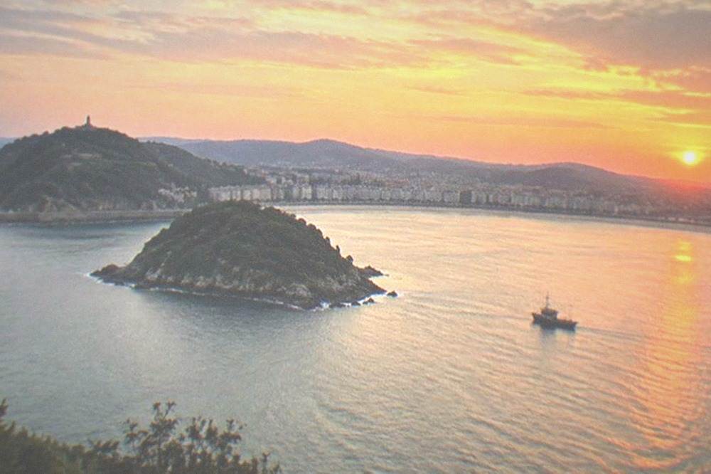 The sun setting over the water of La Concha bay with a boat silhouette and orange sky
