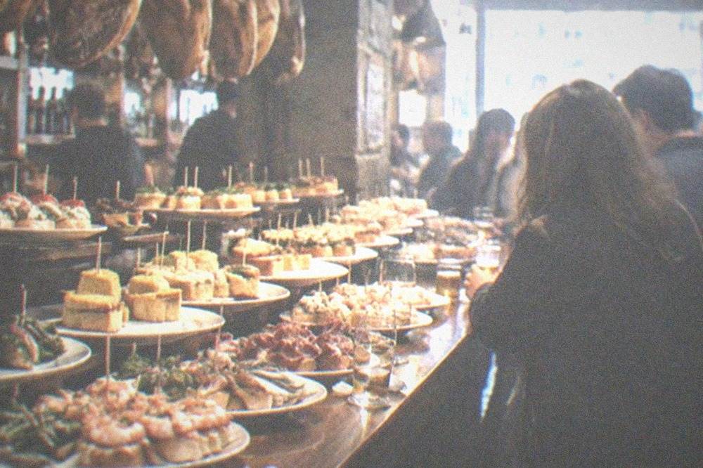 A group standing at a crowded bar counter with pintxo plates