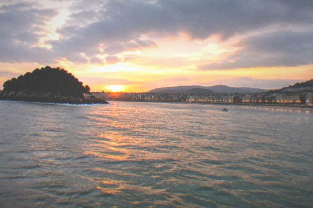 Sunset over La Concha bay seen from the water with the city lights along the promenade