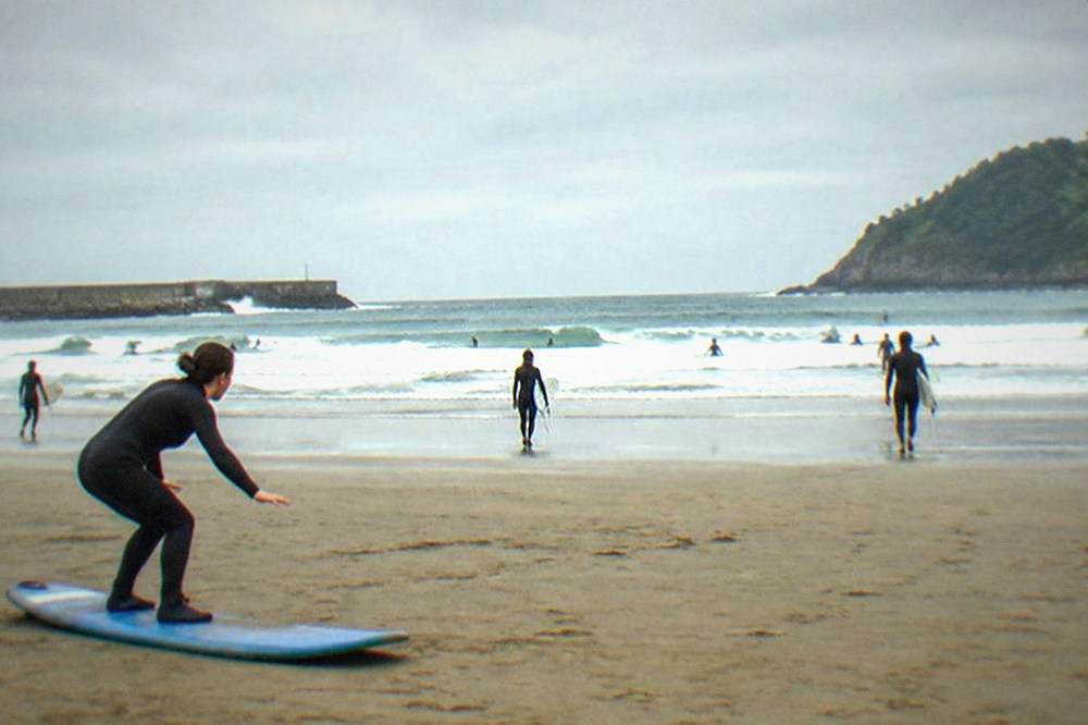 An instructor demonstrating a pop-up stance on a surfboard on the sand