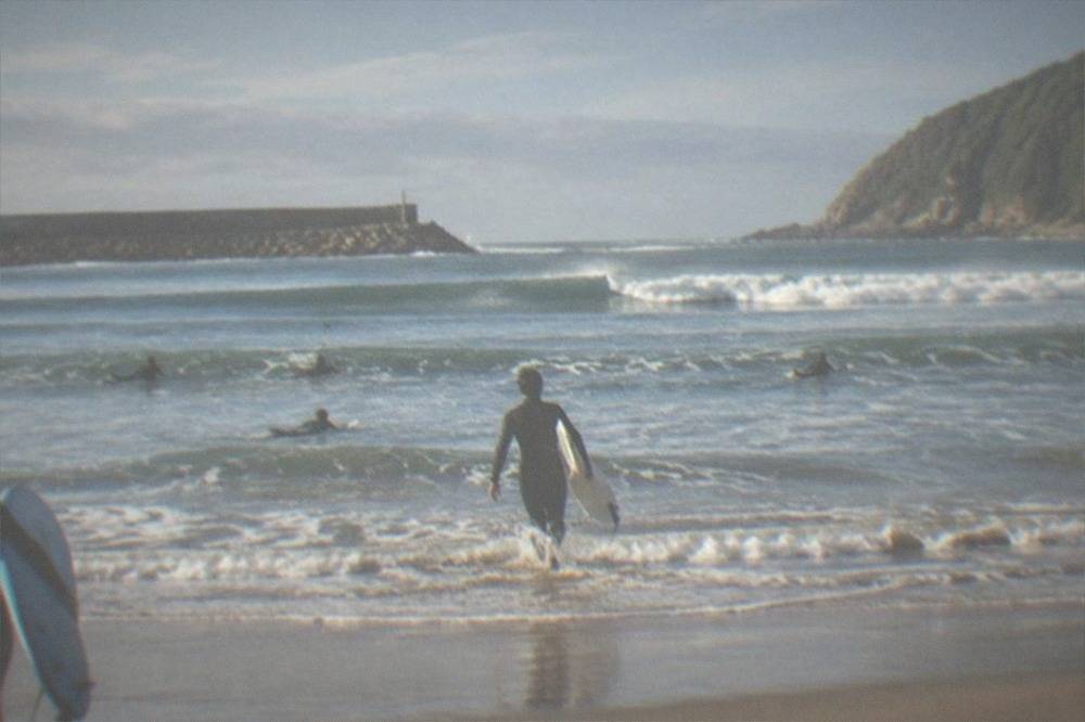 A small group of beginner surfers paddling out at Zurriola beach
