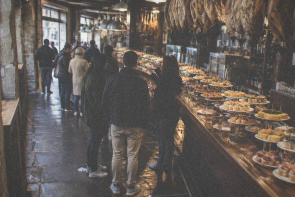 A guide talking to a small group beside a bar counter with pintxos laid out