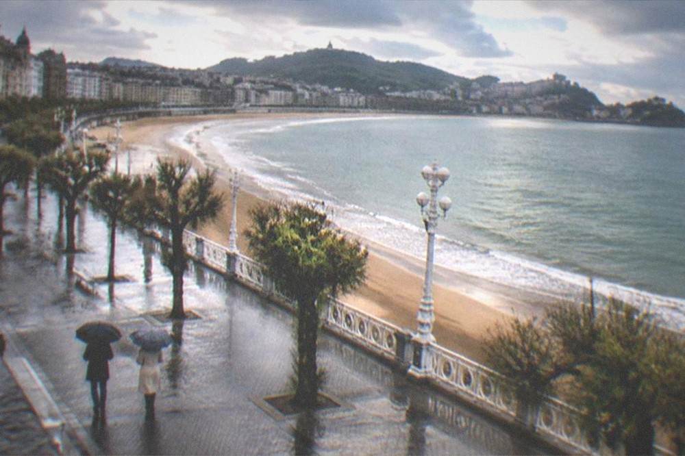 Two people with umbrellas walking a wet seafront promenade past a white railing